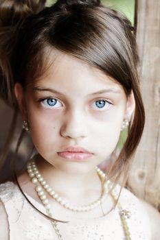 Young girl looking directly into the camera, wearing vintage pearl necklace and hair pulled back. Extreme shallow depth of field with selective focus on eyes.