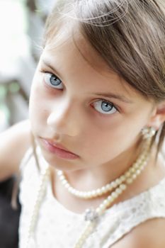 Young girl looking directly into the camera, wearing vintage pearl necklace and hair pulled back. Extreme shallow depth of field with selective focus on eyes.