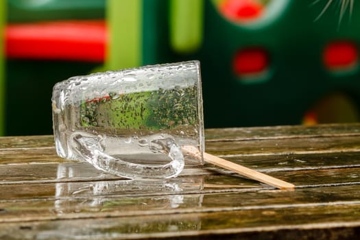 Empty wet glass lying outside on a picnic table after a rain shower. Blurred and colorful background.