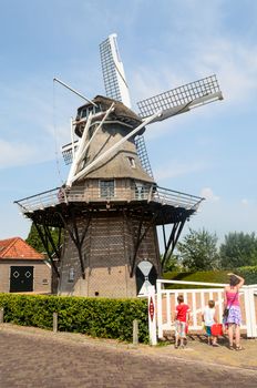 Mother with two young children looking up at a large dutch windmill on a warm and sunny day