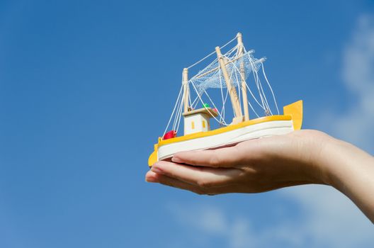 wooden retro ship miniature toy on female palm on blue sky background