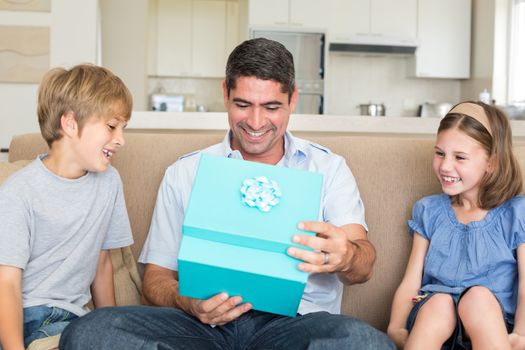 Happy father opening gift given by children on sofa at home