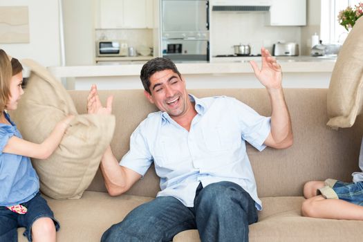 Children hitting father with cushions on sofa at home