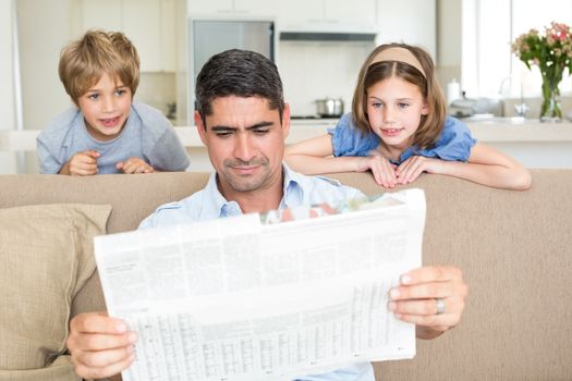 Father and cute children reading newspaper at home