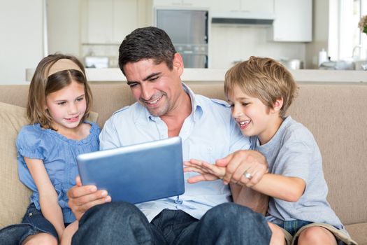 Happy father and children using digital tablet while sitting on sofa at home