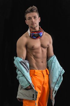 Attractive young male skier or snowboarder taking off jacket on naked muscular torso