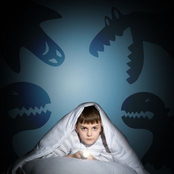 image of a boy under the covers with a flashlight the night afraid of ghosts