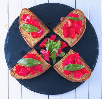 Four bruschetta with tomato and basil over black stone