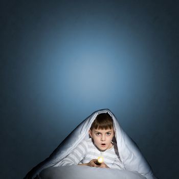 image of a frightened boy under the covers with a flashlight