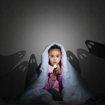 image of a girl under the covers with a flashlight the night afraid of ghosts