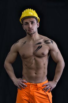 Muscular young construction worker shirtless wearing hardhat, isolated on black background