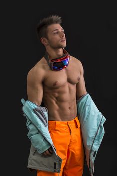 Attractive young male skier or snowboarder taking off jacket on naked muscular torso