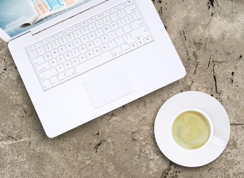 Laptop and a cup of coffee with crema on old concrete surface. Computer technology concept