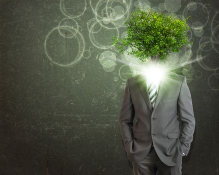 Businessman stand with green tree and bright light instead his head. Eco concept