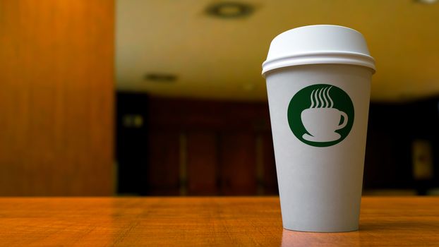 A paper coffee cup in an office or coffee shop setting with a green Starbucks-like logo