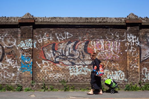 MILAN, ITALY - MAY, 18: Woman walking next to the brick wall painted with graffiti on May 18, 2014