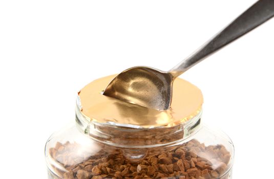 Metal teaspoon breaking the foil seal on a jar of instant coffee granules for the first time, isolated on a white background