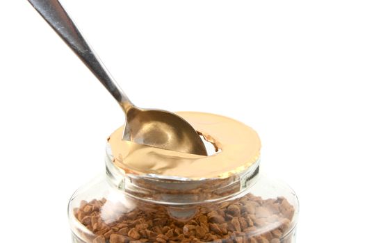Ripping a hole in the foil of a new jar of instant coffee granules with a teaspoon, isolated on a white background