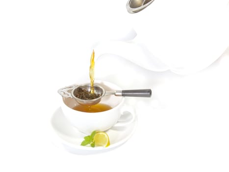 Pouring tea from a Tea Pot into a white cup with lemon and mint