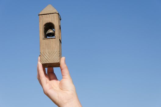 female hand hold old vintage wooden belfry miniature on blue sky background