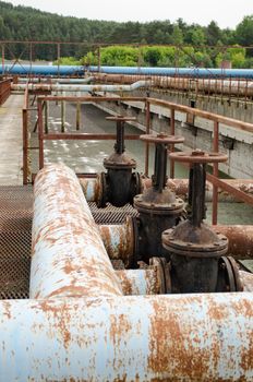 Rusty taps valves gate and pipes in water treatment plant and dirty liquid bubble.