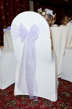 Lilac ribbon and bow decorates chair at wedding reception