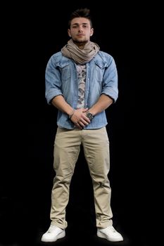 Full length body shot of attractive young man standing on black background, looking at camera