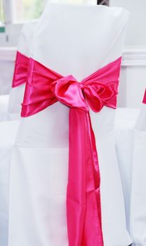 Closeup of white chair cover with red or pink ribbon tied in a bow at wedding