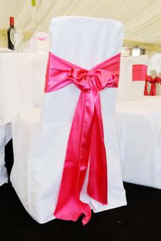 Chair with pink ribbon tied in bow at wedding reception