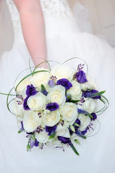 Bride holding bouquet of white rose and purple flowers on wedding day closeup