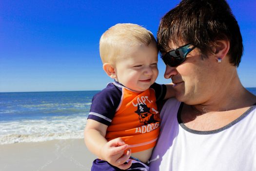 grandfather holding his young grandson at the beach on a sunny day