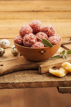 Raw meatballs with sage on warm wooden background