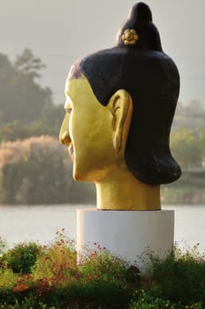 Golden head sculpture in garden near river