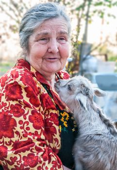 Senior woman holding a goatling on a background of his home