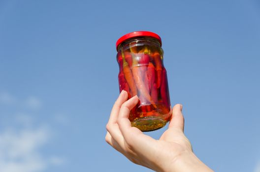 red hot chili pepper glass jar in girl hand on blue sky background
