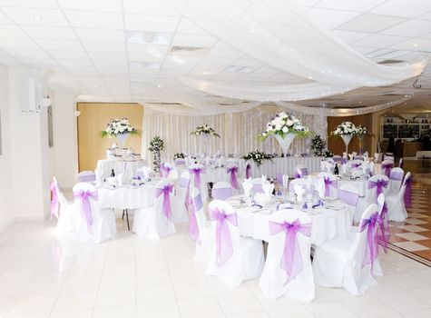 Wedding reception interiot showing tables and chairs decorated in white and purple