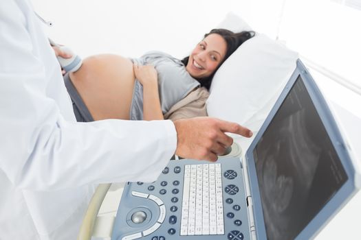 Midsection of male doctor showing ultrasound monitor to pregnant woman in hospital