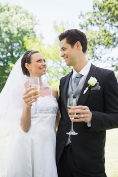 Romantic bride and groom having champagne while looking at each other in park