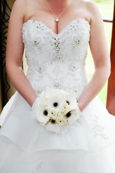 Closeup detail of brides white bouquet and wedding dress