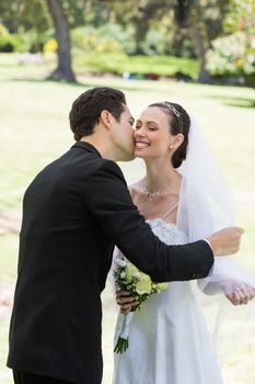 Young romantic groom kissing bride in garden