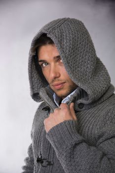 Good looking young man wearing winter hoodie sweater looking at camera