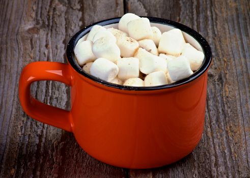 Hot Chocolate in Orange Cup with Marshmallows on Rustic Wooden background