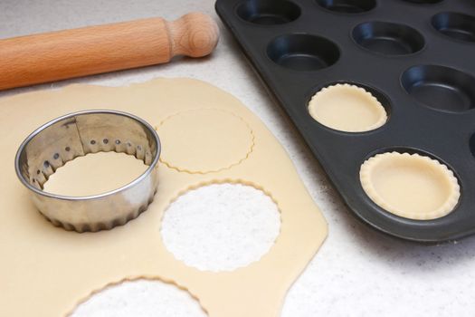 Lining a bun tin with circles of rolled out pastry to make mince pies, with a rolling pin on the worktop