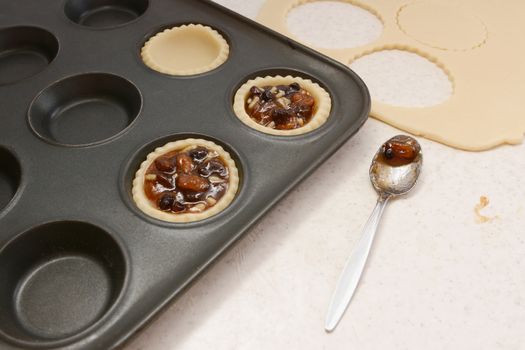 Filling pastry cases with mincemeat, with a used teaspoon on worktop