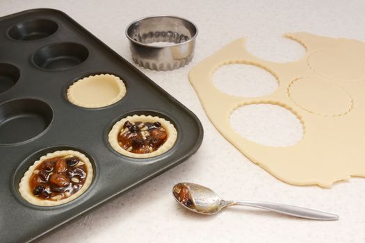 Producing mince pies, cutting pastry circles with cutter and filling with mincemeat