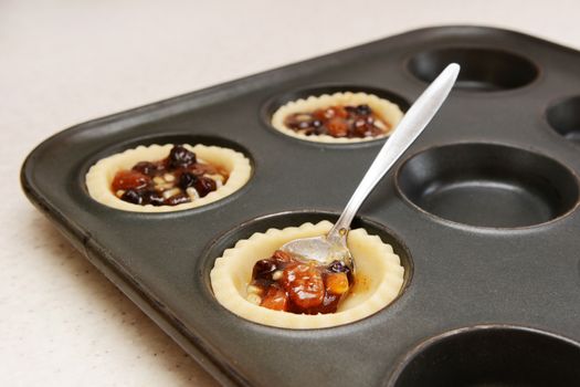 Spooning mincemeat into pastry cases in a bun tin with a teaspoon