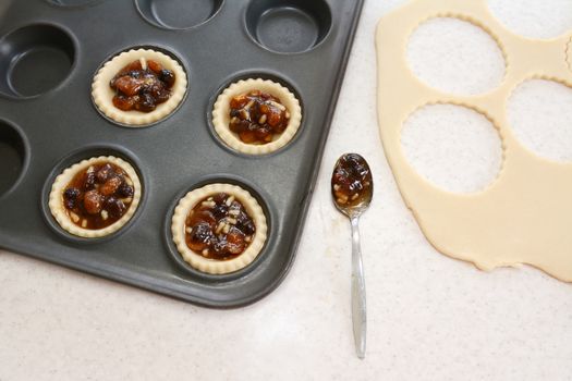 Making mince pies in the kitchen - filled pastry cases, mincemeat, dough scraps and teaspoon