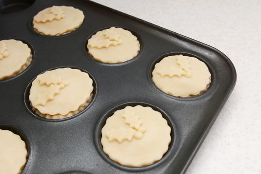 Mince pies in a bun tin ready for the oven, with pastry holly leaf decoration
