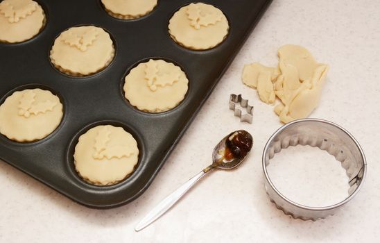 Uncooked mince pies in a bun tin, pastry leftovers, teaspoon and cutters