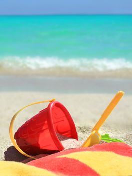       Beach toys and towel in red and yellow in  sand on a tropical Caribbean beach with blue ocean in the background      